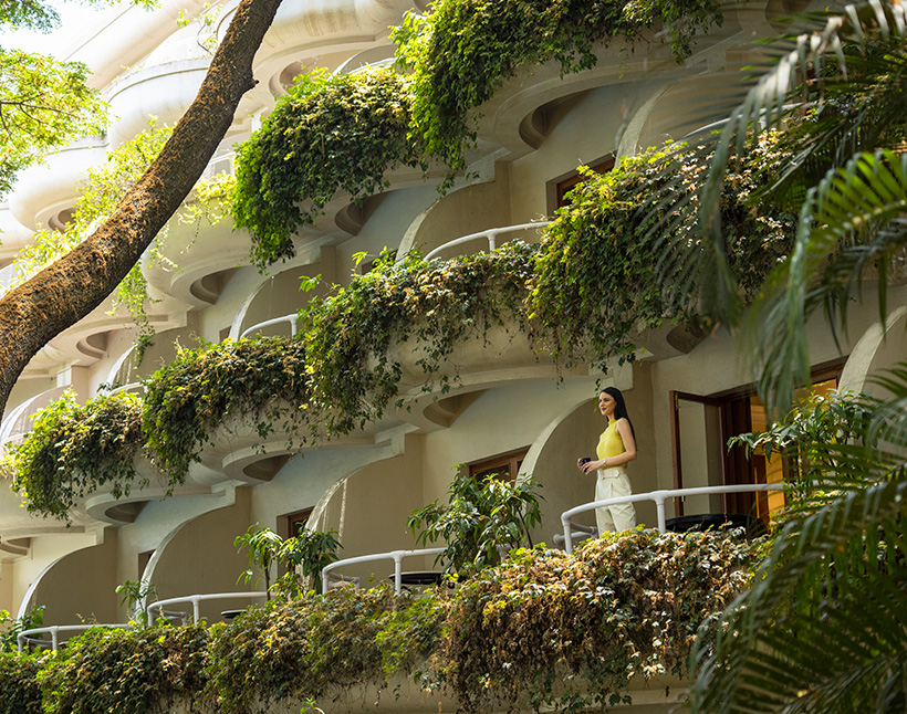 The Oberoi Bengaluru balcony with greenery and woman enjoying view.