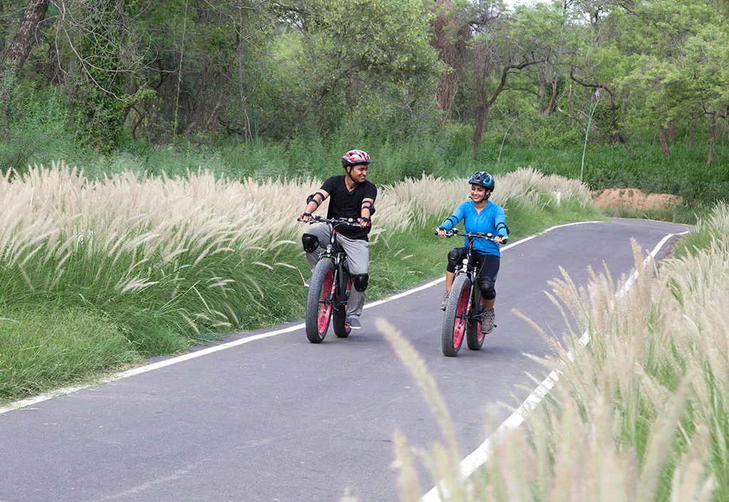 Two people cycling on a forest path near The Oberoi Sukhvilas