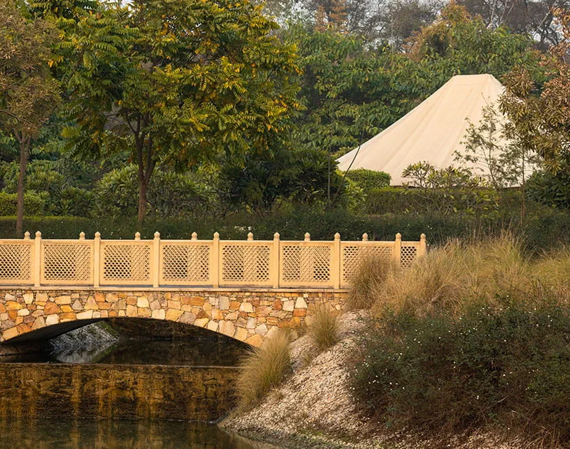 Stone bridge and tent amidst lush greenery at The Oberoi Sukhvilas