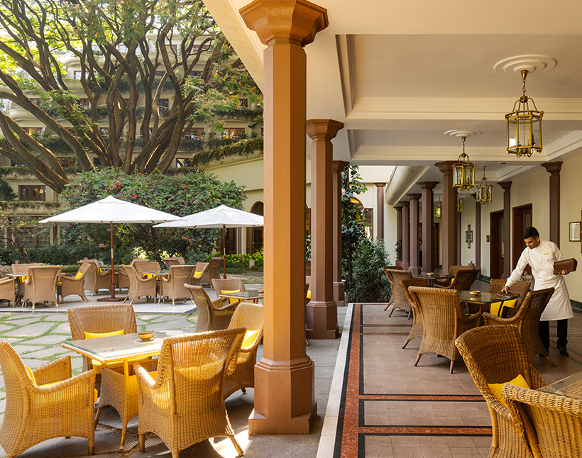 Hotel Oberoi Bengaluru outdoor seating with waiter arranging chairs.