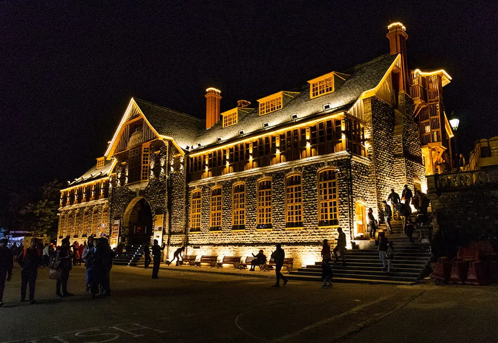 Illuminated historic building in Shimla at night with people outside