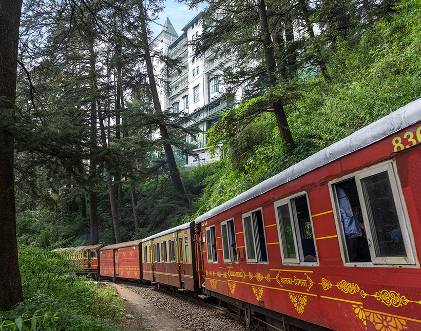 Red train passing through forest near luxury hotel, the Oberoi Cecil