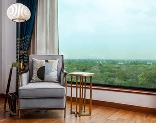 Armchair and table by large window overlooking greenery, The Oberoi New Delhi