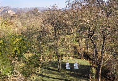 Two people meditating outdoors beneath trees at The Oberoi Sukhvilas