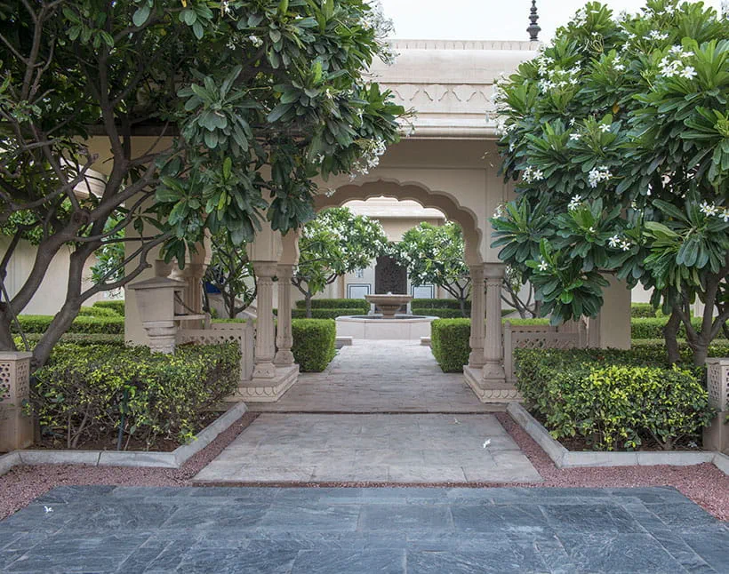 An elegant archway leads to fountain at The Oberoi Sukhvilas, surrounded by lush green trees and hedges, creating a serene ambiance in this 5-star resort at Siswan Forest Resort